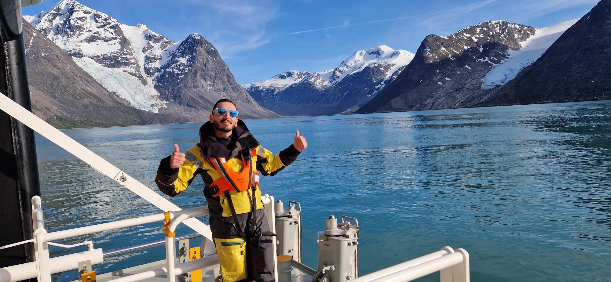 Man standing infront of mountains in Greenland on a boat