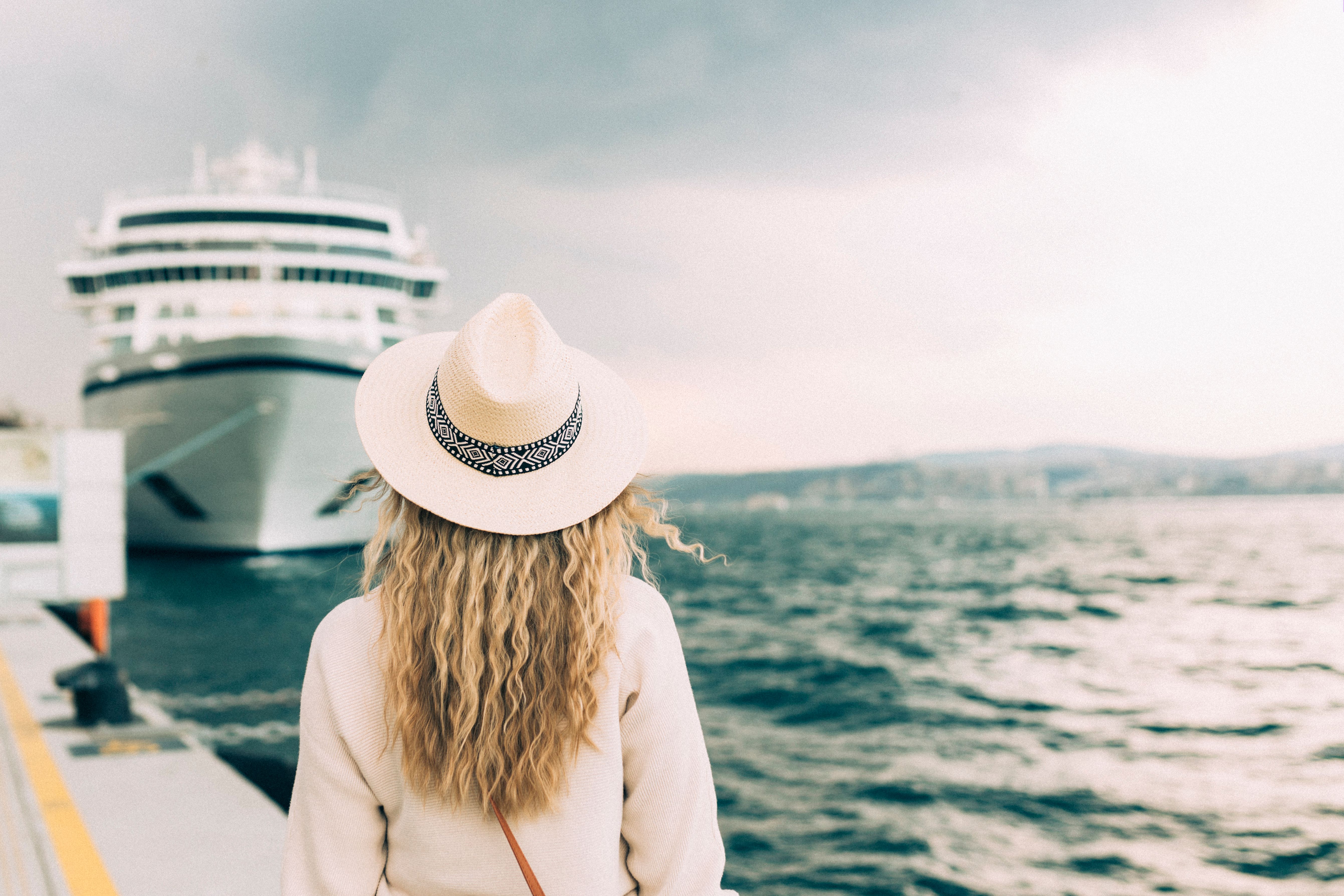 Woman with hat facing cruise ship in port